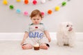 Happy surprised cute Caucasian baby boy celebrating his first birthday at home. Child kid sitting on floor with pet dog. Tasty Royalty Free Stock Photo