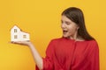 Happy surprised girl holds model of house on palm on bright orange background. Real estate as gift. Winning apartment