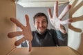 Happy and surprised man is opening a gift and looking inside cardboard box.