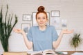 Happy surprised redhead young woman student sitting at a table with textbooks and a workbook Royalty Free Stock Photo