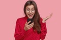 Happy surprised sociable lady looks positively at screen of cell phone, recieves good news, uses modern technologies Royalty Free Stock Photo