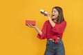 Happy surprised young woman with an open gift box and looks admiringly into it. Girl received gift. Yellow background