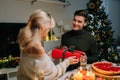 Happy surprised young woman receiving gift box from loving man sitting at dinner table at home on Christmas Eve near Royalty Free Stock Photo