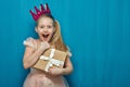 Happy surprising girl wearing pink dress and crown holding gift