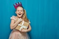 Happy surprising girl wearing pink dress and crown holding gift