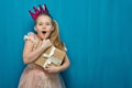 Happy surprising girl wearing pink dress and crown holding gift