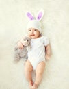 Happy sweet baby in knitted hat with a rabbit ears and teddy bear on bed