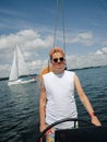 Happy tattooed adult person steering a sailboat during his yacht voyage in a sunny summer day and sailboat on a lake on a