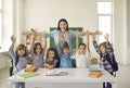 Happy teacher with arms widely spread to hug cheerful children raising hands Royalty Free Stock Photo