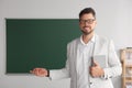 Happy teacher with book explaining something at blackboard in classroom Royalty Free Stock Photo