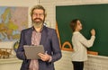 Happy teacher and child in classroom. change of duties. bearded man make notes in clipboard. little girl write answer on