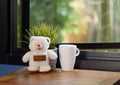 A happy teddy bear and white coffee cup sit on wood table with window open background Royalty Free Stock Photo