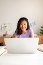 Happy teen asian female high school student studying at home, doing homework using laptop looking at camera. Vertical. Royalty Free Stock Photo