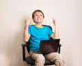 Happy teen boy with laptop in winning pose. Success kid in office chair with portable pc happy ecstatic celebrating being Royalty Free Stock Photo