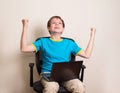 Happy teen boy with laptop in winning pose. Success kid in office chair with portable pc happy ecstatic celebrating being Royalty Free Stock Photo