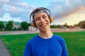 Happy teen boy portrait at a sport stadium, he`s wearing headphones and smiling, a soccer field with green grass - sports and