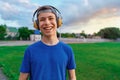 Happy teen boy portrait at a sport stadium, he`s wearing headphones and smiling, a soccer field with green grass - sports and