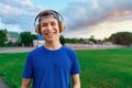 Happy teen boy portrait at a sport stadium, he`s wearing headphones and smiling, a soccer field with green grass - sports and