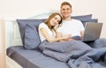 Happy teen couple using laptop on bed at bedroom. Young married couple lying on bed at home and using laptop Royalty Free Stock Photo