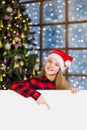 Happy teen girl in christmas hat peeking above white banner and pointing down. Space for text Royalty Free Stock Photo