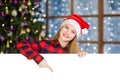 Happy teen girl in christmas hat peeking and pointing down at empty board. Space for text Royalty Free Stock Photo