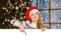 Happy teen girl in christmas hat peeking and pointing down at empty board. Space for text Royalty Free Stock Photo