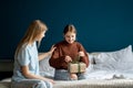 Happy teen girl daughter sitting on bed opening wrapped gift box, receiving present from mother Royalty Free Stock Photo