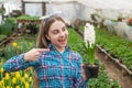 happy teen girl florist in greenhouse. spring and summer. pointing finger on pot plants. Royalty Free Stock Photo