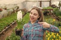 happy teen girl florist in greenhouse. spring and summer. pointing finger on pot plants. Royalty Free Stock Photo