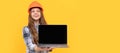 happy teen girl in helmet and checkered shirt presenting computer, presentation. Child builder in helmet horizontal