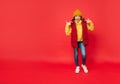 happy teen girl in knitted hat pointing finger on herself on red background, copy space, winter. Royalty Free Stock Photo