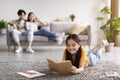 Happy teen girl lies on floor and reads book, selective focus. Young asian man and woman resting on sofa Royalty Free Stock Photo