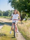 Happy teenage girl with long hair riding bicycle in field at sunny day Royalty Free Stock Photo