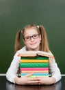 Happy teen girl with pile books near empty green chalkboard