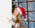 Happy teen girl in red christmas hat peeking above white banner and pointing away Royalty Free Stock Photo