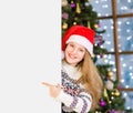 Happy teen girl in red christmas hat peeking and pointing at empty board Royalty Free Stock Photo