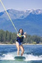 Happy teen girl wake boarding at a picturesque mountain lake on her summer vacation. Boating lifestyle