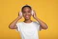 Happy teen pretty afro american girl in white t-shirt in headphones listening music, isolated on yellow background Royalty Free Stock Photo