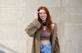 Happy teen redhead girl looking at camera standing on urban wall background. Royalty Free Stock Photo