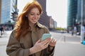 Happy teen redhead girl standing on big city urban street using smartphone. Royalty Free Stock Photo