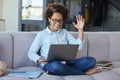 Happy teen schoolgirl wearing earphones looking cheerful while using laptop, greeting friends and teacher during online