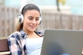 Happy teen wearing headphones using laptop on bench