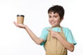 Happy teenage boy, bartender in chef apron selling coffee in an eco cardboard cup, isolated on white. Hot drink to go