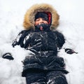 Happy teenage boy dressed in warm winter jacket with fur hood lies in the snow. Winter fun. Royalty Free Stock Photo