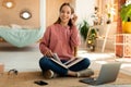 Happy teenage female student in headphones reading book during online class near laptop computer, sitting at home Royalty Free Stock Photo