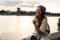 Happy teenage female tourist sitting on sea promenade of an old city in sunset. Young woman world traveler singing her favorite Royalty Free Stock Photo