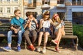 Happy 4 teenage friends or high school students are having fun, talking, reading phone, making selfie photo in city on bench. Royalty Free Stock Photo