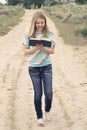 Happy teenage girl reading a book while walking down a dirt road