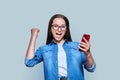 Happy teenage girl with smartphone, emotion yes success on gray background Royalty Free Stock Photo