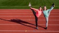 Happy teenage gymnasts do vertical splits holding legs at athletics track, copy space, gymnastics